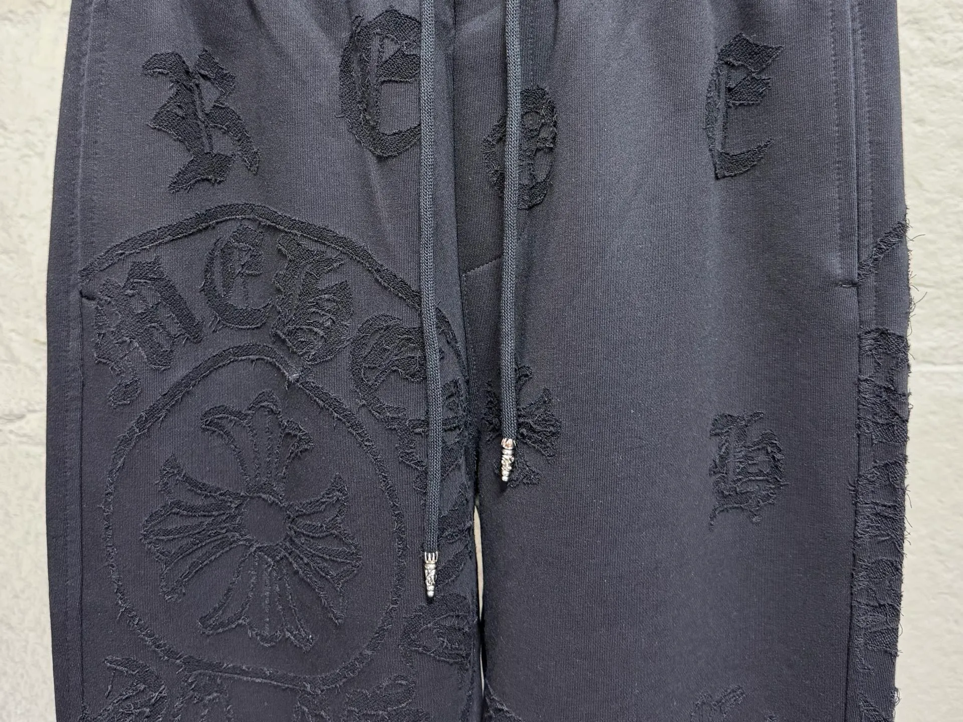 CH/Cro Heart 2026ss Burnt Flower Straight-leg Sweatpants Classic heavy-weight sweatpants with gray tones, Retro street style full-fitting, direct recognition, same style for men and women. ●Three-dimensional patchwork technology: The whole body is covered with Gothic letters + cross flower totems, using raw edge patchwork embroidery, with a mustache-like old texture, and uneven and layered patterns. It is not an ordinary print, and it is durable and not easy to fall off. ●Style tailoring: Loose, straight and wide-legged version, modifying the shape of the legs, hiding the flesh neatly, not flattering the figure, with an online drape, and the upper body has a relaxed street tone. ●Fabric and waist: Heavy knitted terry fabric, thick and soft, with good drape; elastic drawstring waist, with branded metal engraved rope ends, easy to put on and take off, and strong waist adaptability. ●Detailed design: The side pockets are convenient for carrying items, and the back pocket is decorated with cross-pattern patches. The front and rear patterns echo each other. Every detail is highly recognizable to the brand. ●Wearing scenarios: Suitable for street wear, daily outings, and trendy wear. Paired with sweaters, denim jackets, and leather jackets, you can easily create an American retro cool style. ●The overall gray base is paired with Cream White patches, which are low-key yet impactful. They are both comfortable and trendy. Versatile sweatpants, a must-have for fashionistas, are also available at the counter. SIZE：M L XL XXL XXXL
